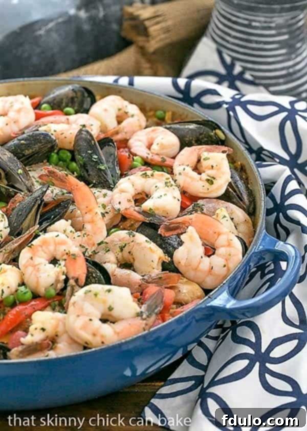 Julia Child's American Paella 2 Julia Child's Paella a l'Americaine in a cast iron paella dish on a blue and white patterned napkin, ready to be served.