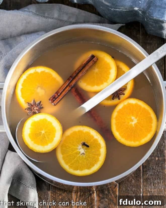 Hot Apple Cider Recipe - Hot cider flavored with vanilla, oranges and warm autumn spices. Perfect for holiday parties, apres ski parties or anytime you need to warm your soul Mulled Apple Cider simmering in a large stock pot, showcasing orange slices and various whole spices infusing their flavors, creating an inviting aroma.
