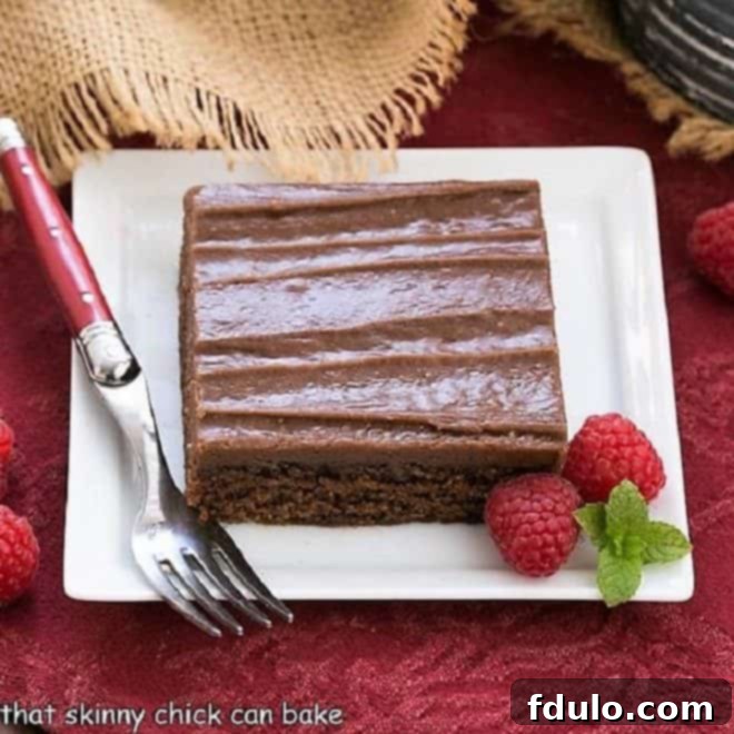 A perfectly sliced piece of Chocolate Sheet Cake, rich and fudgy, presented on a pristine white square plate and garnished with vibrant red raspberries, inviting indulgence.