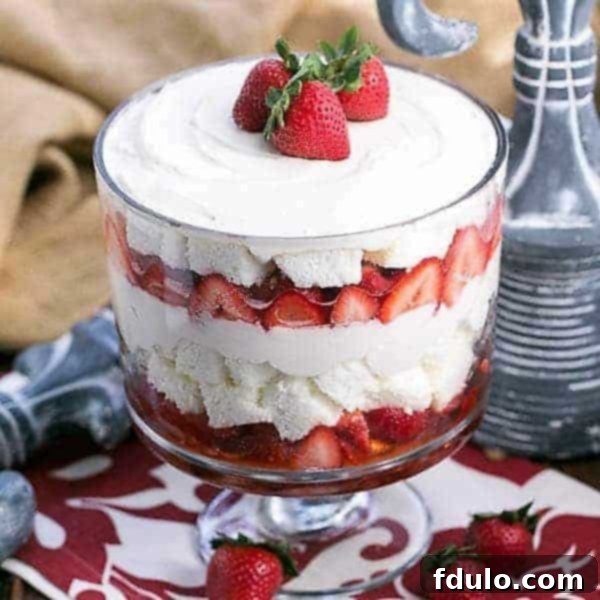 A beautifully layered Strawberry Cheesecake Trifle in a clear glass trifle bowl, garnished with whole fresh strawberries on top.