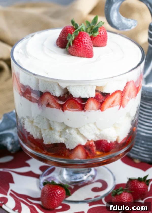 A close-up view of the Strawberry Cheesecake Trifle showcasing its beautiful layers of cake, cheesecake, and strawberries, topped with three whole fresh strawberries.