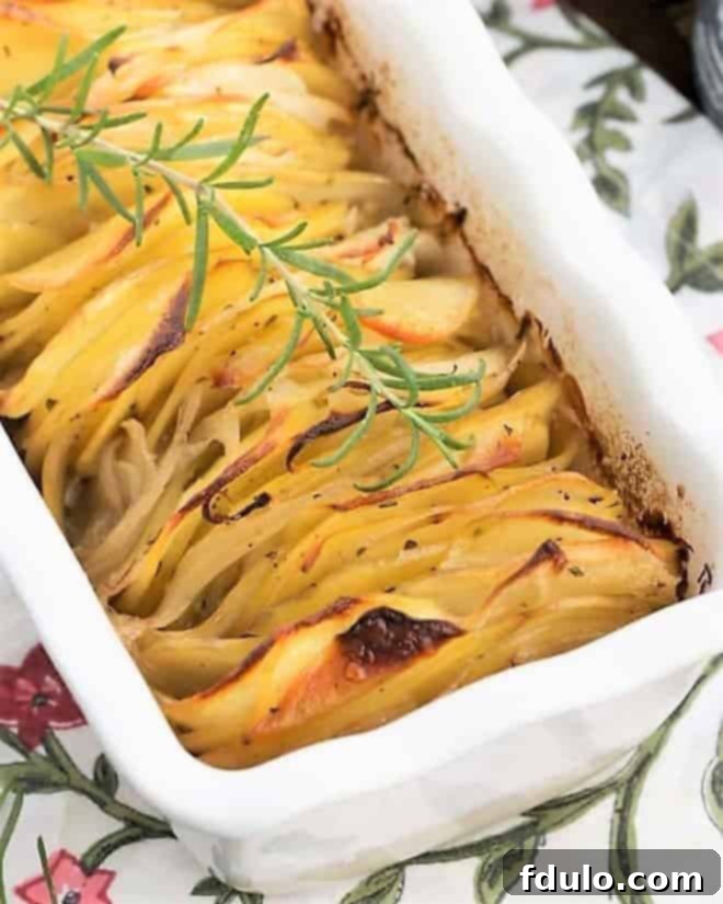 Hasselback Potato Casserole - a captivating and flavorful side dish. Close view of a hasseback potato casserole with a sprig of rosemary in a white baking dish, ready to be served.