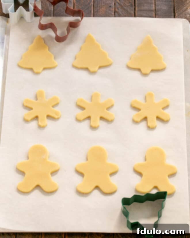Dough cut into festive shapes using cookie cutters, placed on a baking sheet with parchment paper.