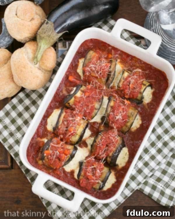 Eggplant Rollatini - A delightful vegetarian entree featuring grilled eggplant rolled around a ricotta mozzarella filling Eggplant Rollatini in a white casserole dish surrounded by wheat rolls and a whole eggplant