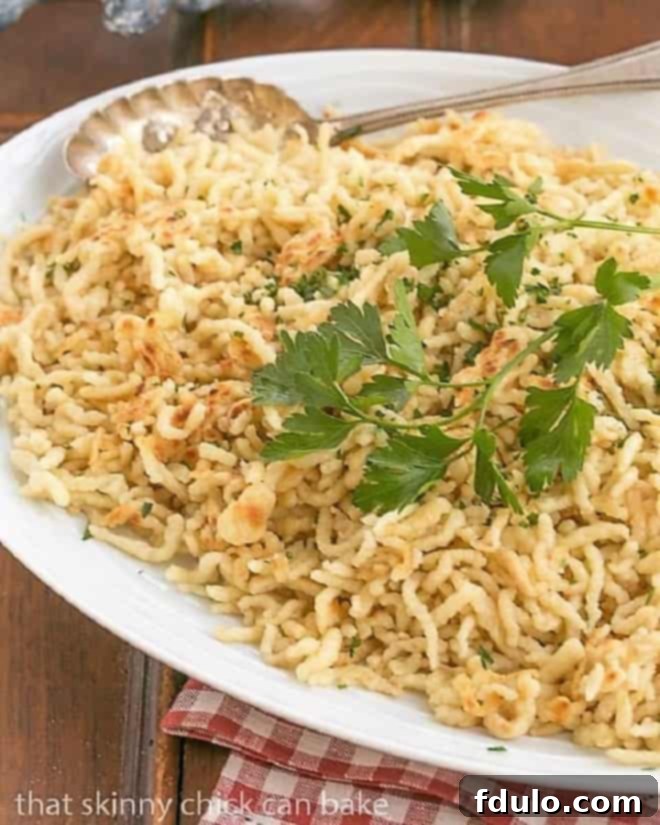Spaetzel topped with a fresh parsley sprig on a white platter, highlighting its delicious texture.