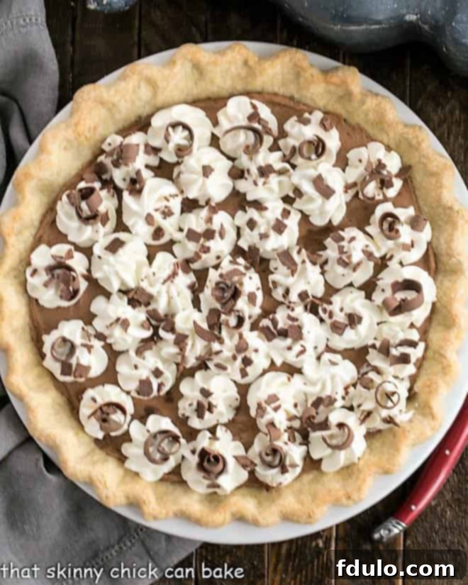 Overhead view of a beautiful Frangelico French Silk Pie in a vibrant red ceramic pie plate, adorned with swirls of whipped cream and delicate chocolate garnishes, ready to be served.