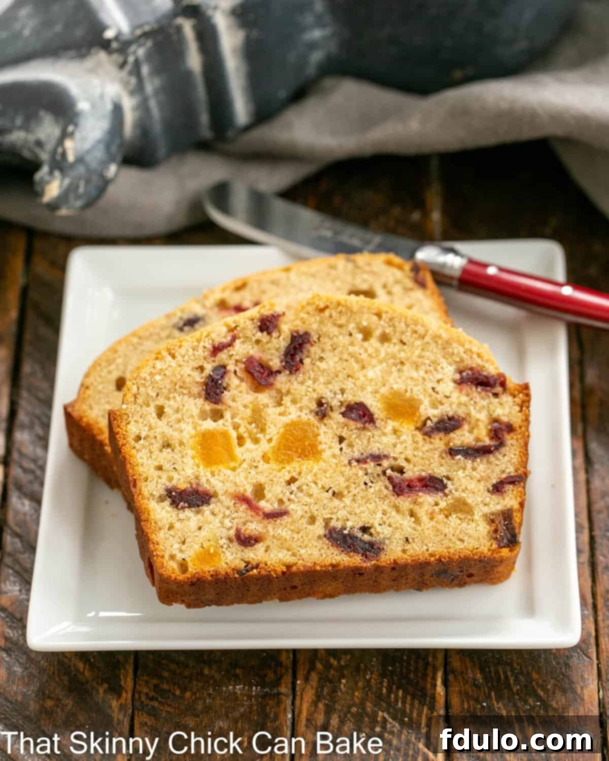 2 slices of apricot bread on a square white plate with a red handle knife.