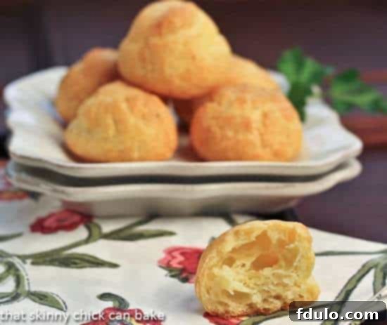 Parisian Cheese Puffs on a white plate with a half cheese puff in the foreground