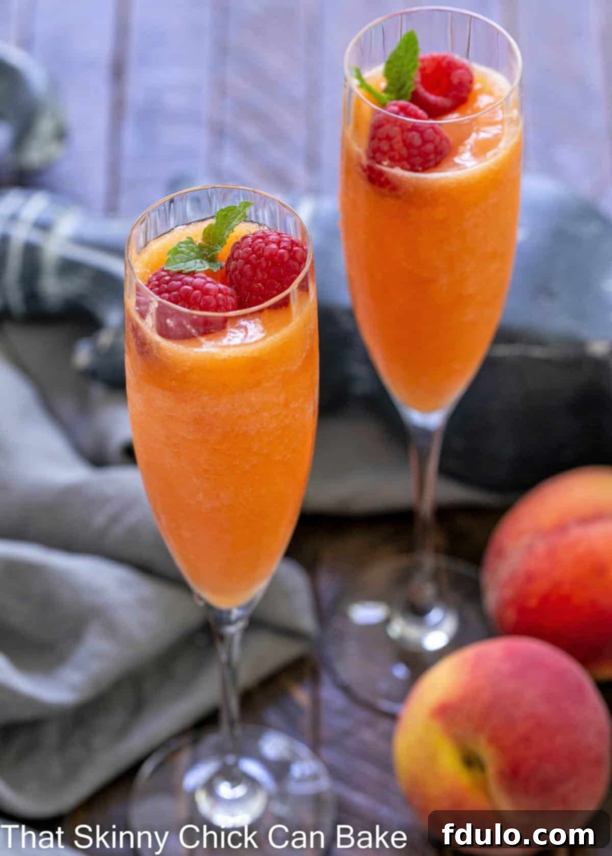 Effervescent Peach Bliss 2 Two beautiful Bellinis in stemmed champagne glasses, garnished with fresh raspberries and a sprig of mint, ready to be enjoyed.