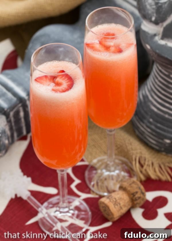 Peach Bellini Cocktail - A slushy version of the famous Italian champagne cocktail Three elegant Peach Bellini cocktails served in flutes, garnished with fresh strawberry slices, radiating a delicate pink hue.