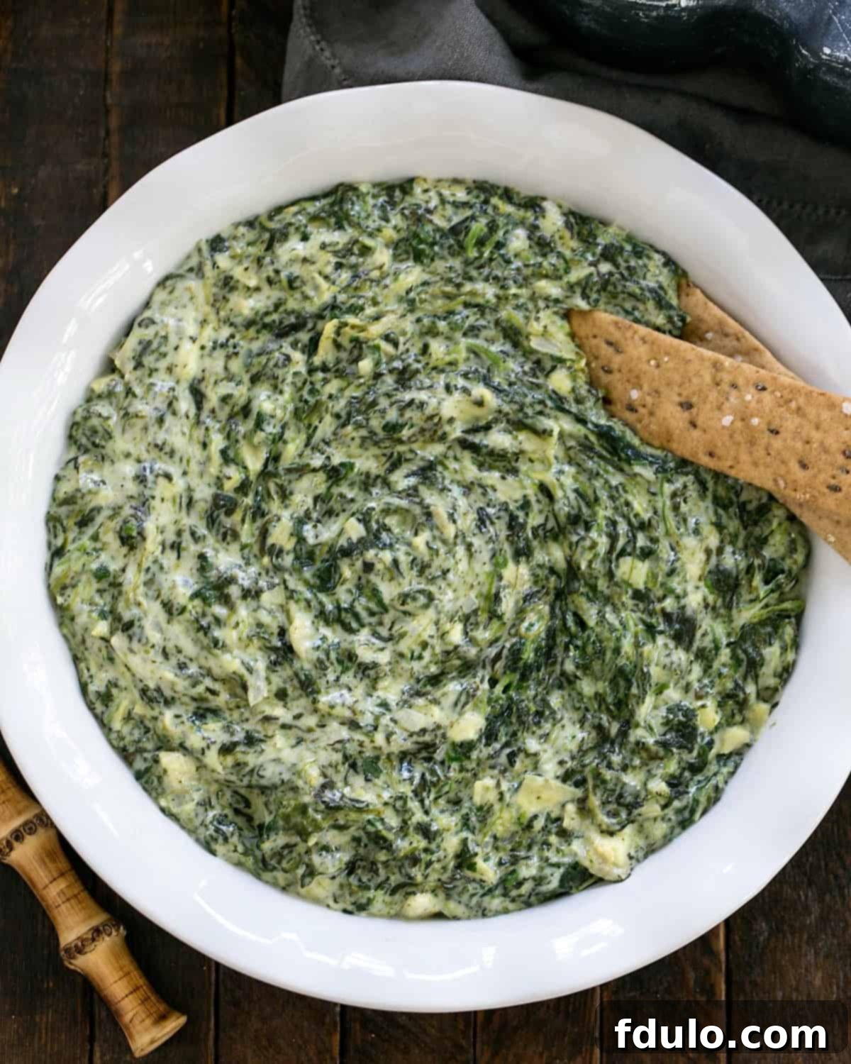 The ultimate Cheesy Spinach Artichoke Dip recipe, served hot and bubbly in a casserole dish. A perfect warm dip for any gathering! Overhead view of a white casserole dish filled with bubbling, warm Spinach Artichoke Dip, garnished with fresh herbs for serving.