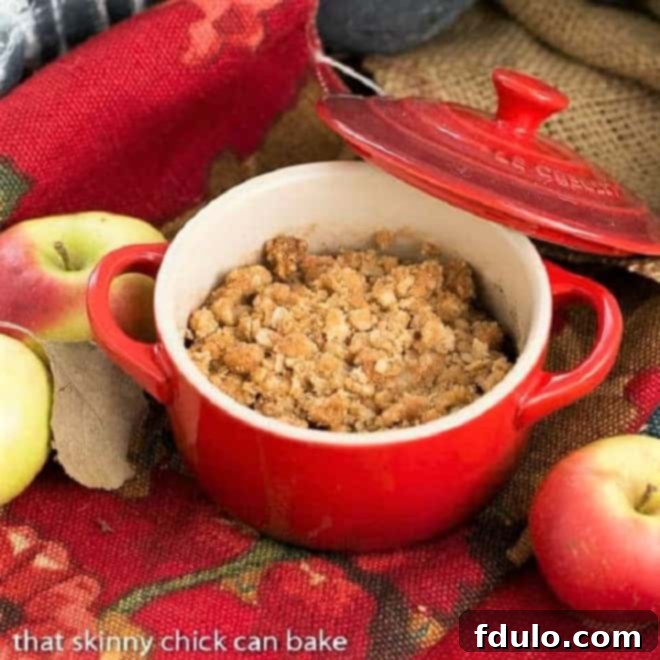 A small red crock filled with a freshly baked Apple Pear Crisp, showcasing its golden, bubbly topping.