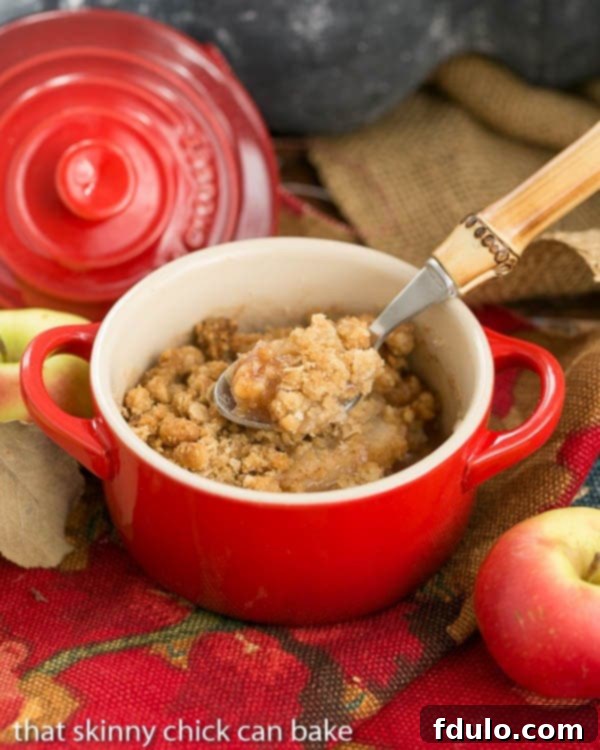 A vibrant Apple Pear Crisp in a red ramekin, served with a elegant bamboo handle spoon, ready to be savored.