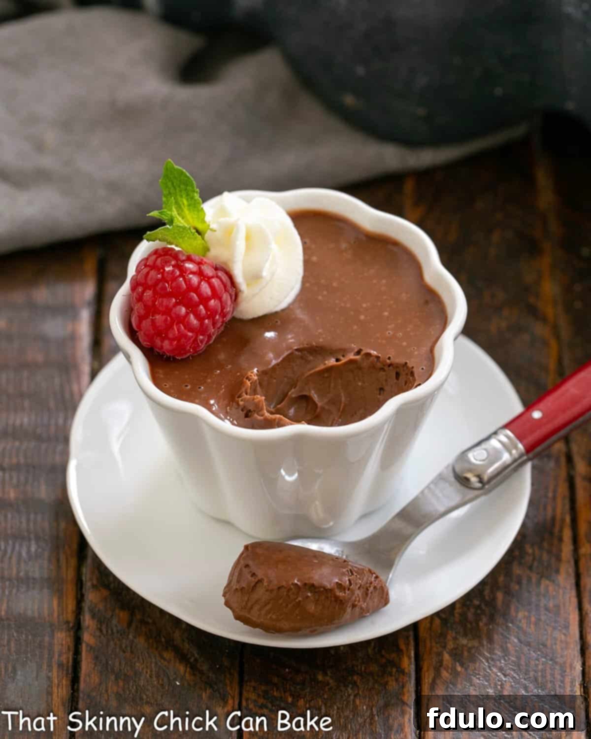 A single serving of Irish cream pots de creme in a pristine white ramekin, with a small spoonful gently removed, showcasing its smooth and creamy texture. Garnished lightly with whipped cream and a raspberry.