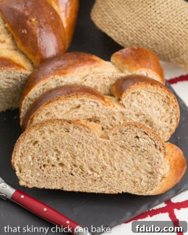 Three perfectly sliced pieces of Whole Wheat Challah on a slate tray, accompanied by a red-handled butter knife.