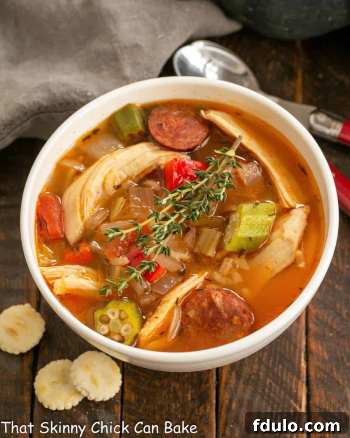 Overhead view of a steaming bowl of Chicken Jambalaya Soup garnished with fresh parsley and served with oyster crackers.
