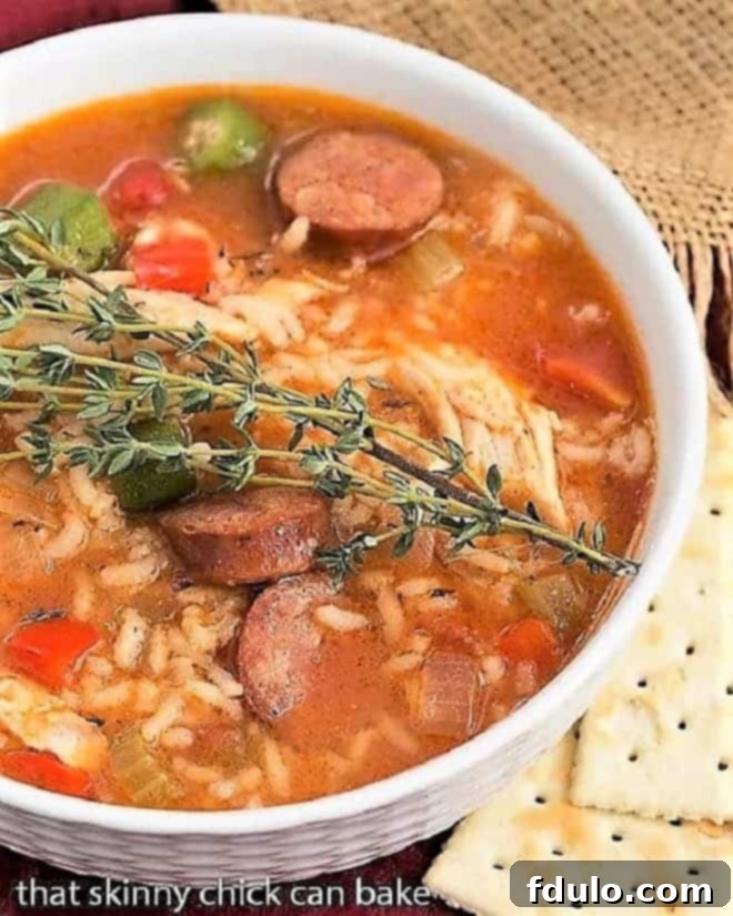 Bowl of Chicken Jambalaya Soup topped with a sprig of thyme and oyster crackers on the side