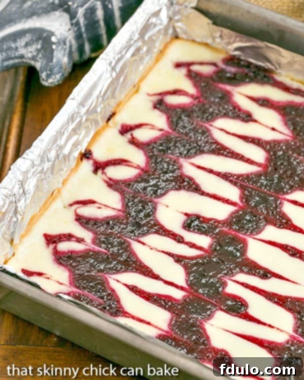Blackberry Swirl Cheesecake Bars are sublime baked cheesecake bars with swirls of blackberry jelly. I gently swirled some homemade jelly into the batter to create these luscious Blackberry Cheesecake Bars. It's one of my favorite baked cheesecake dessert recipes. A baking pan filled with freshly baked Blackberry Swirl Cheesecake Bars, showing the intricate swirls of blackberry jelly throughout the creamy cheesecake layer.
