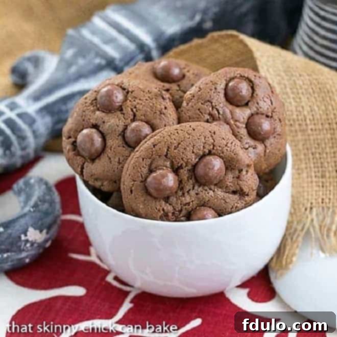 A bowl filled with freshly baked Whopper Cookies, highlighting their chocolatey texture and visible malted milk ball pieces, resting on a charming red and white napkin.