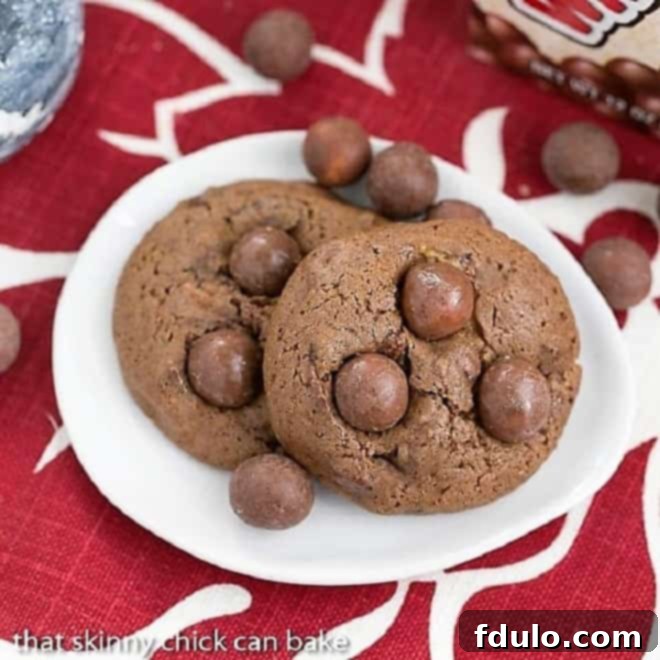 An overhead view of a collection of perfectly baked Chocolate Malt Cookies, featuring visible malted milk ball pieces, neatly arranged on an elegant oval white plate.