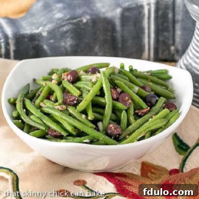 Side view of vibrant mustard green beans in a white serving bowl, garnished with olives