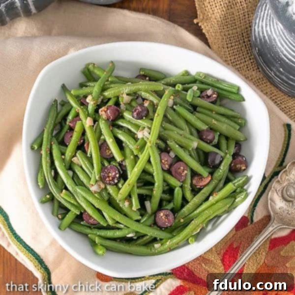 Overhead view of a bowl of vibrant green mustardy haricots verts, showcasing the olives and dressing