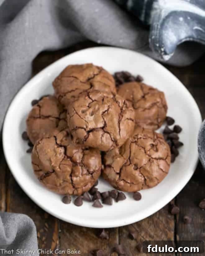 A stack of Chocolate Brownie Cookies with Mini Chocolate Chips on a white plate, garnished with additional chips.