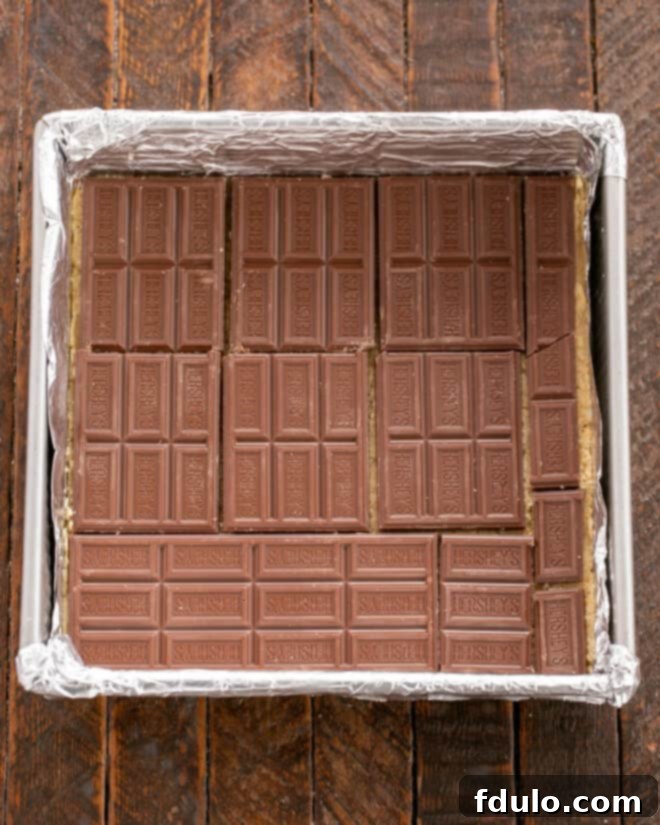 Step 5: Arranging standard-sized Hershey's milk chocolate bars in a single layer over the pressed cookie dough base.
