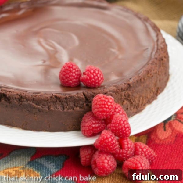 Flourless Chocolate Torte with Raspberry Sauce - A decadent gluten free flourless chocolate torte topped with chocolate ganache A beautiful cake platter elegantly displaying an entire Flourless Chocolate Torte, generously topped with glossy chocolate ganache.