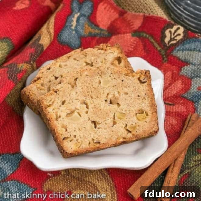 Slices of moist Cinnamon Spiced Apple Bread on a white plate with cinnamon sticks, perfect for a cozy autumn treat.