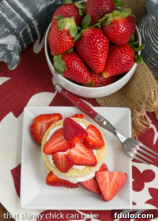 Overhead image showcasing individual olive oil cake rounds meticulously topped with sweetened whipped cream and vibrant, ripe, juicy strawberry slices, ready to be served.