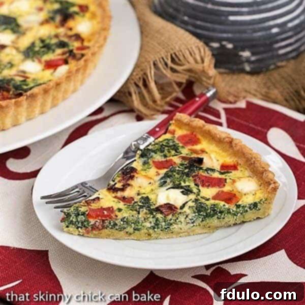 Sun-dried Tomato and Spinach Quiche - A Memorable Mediterranean Quiche Slice A perfectly sliced Sun-dried Tomato and Spinach Quiche, revealing layers of vibrant red tomatoes and green spinach, served on a pristine white plate with a red-handled fork.