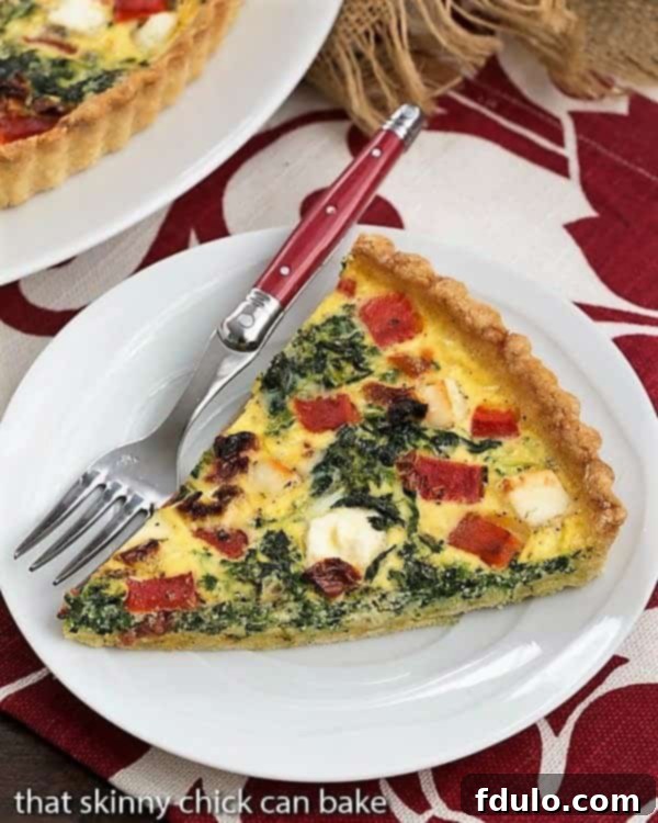 Sun-dried Tomato and Spinach Quiche - Slice on a Plate A beautiful slice of Sun-dried Tomato and Spinach Quiche resting on a white plate, set against a charming red and white patterned napkin.