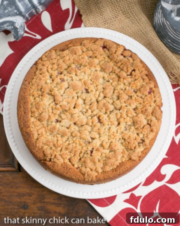 An overhead view of a whole raspberry coffee cake on a white serving platter, showcasing the streusel topping and ruby-red berries.