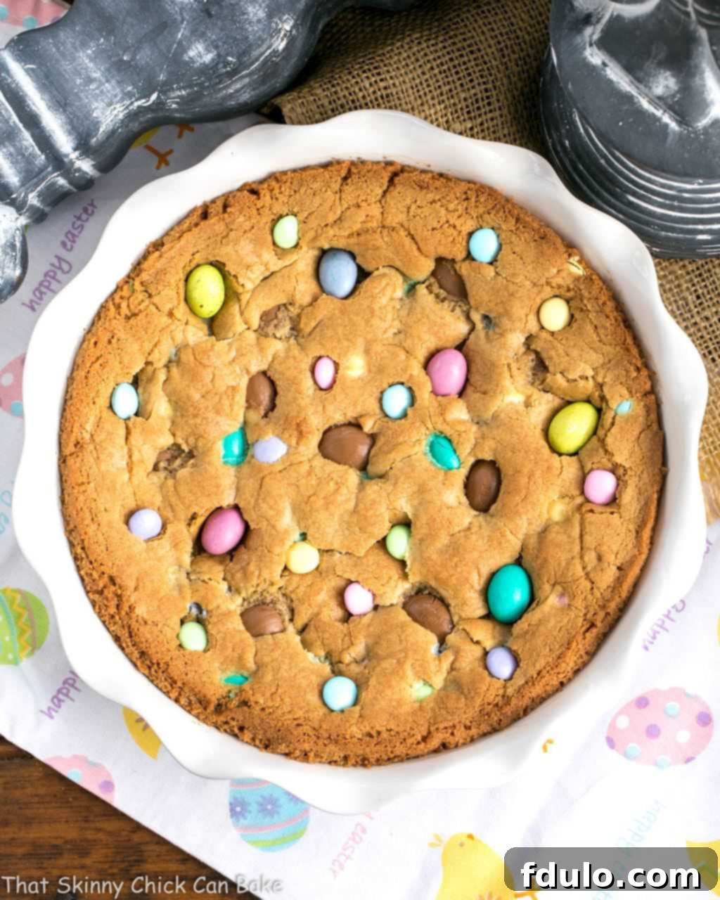Easter Cookie Cake Recipe - Packed full of Easter candy and chocolate chips, wedges of this big cookie will be a guaranteed hit! An inviting overhead shot of a large, freshly baked Easter cookie cake, generously studded with a vibrant assortment of Easter candies, including colorful M&M's and mini Cadbury eggs.