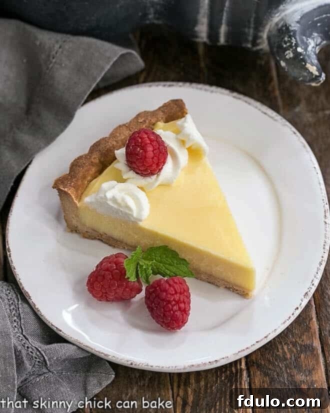 A perfectly sliced piece of Creamy Lemon Tart presented on a white dessert plate, showcasing its pristine filling.