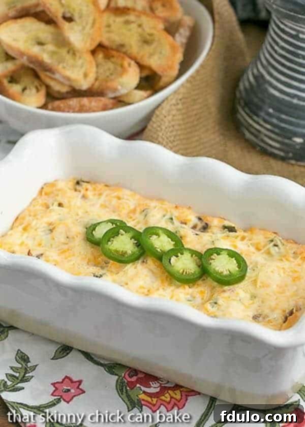 Jalapeno Popper Dip in a white ceramic loaf pan, garnished with fresh sliced jalapenos and served with crackers.