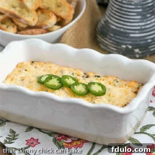 Jalapeno Popper Dip in a loaf pan, freshly baked and topped with bright green sliced jalapenos, ready to be served.