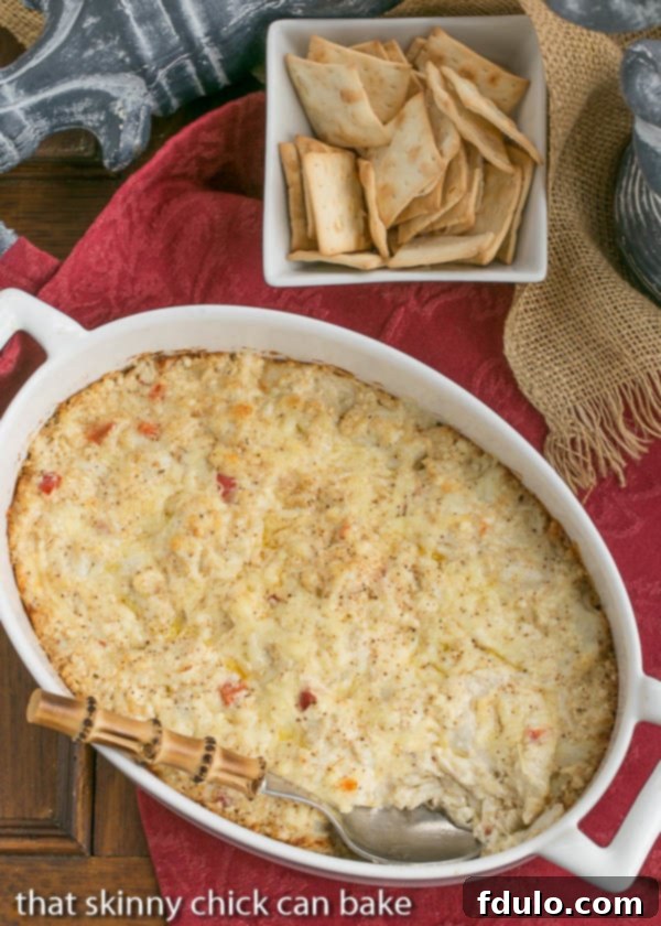 Luxurious Cheesy Crab Dip with lump crab meat, served warm in a white ceramic dish, garnished with fresh herbs.