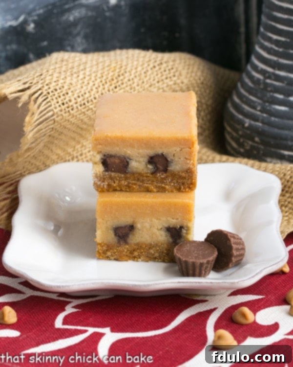 Stacked Peanut Butter Cheesecake Bars on a white square dessert plate, showing layers of crust, peanut butter cups, cheesecake, and ganache.