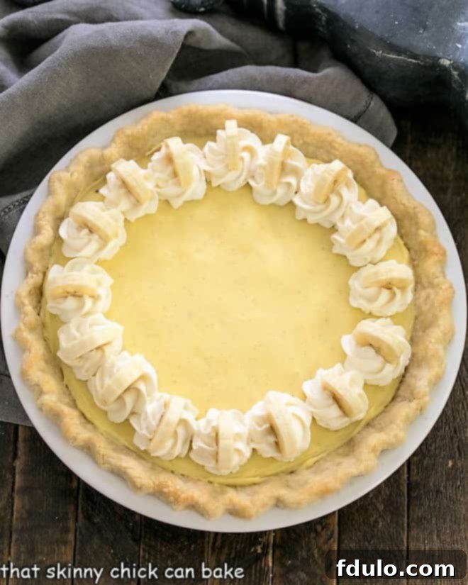 Overhead view of a perfectly crafted banana cream pie, generously garnished with fresh whipped cream and delicate banana slices, ready to be served.