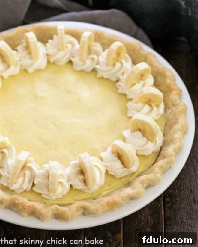 A tantalizing partial overhead view of a banana cream pie, beautifully garnished with delicate swirls of whipped cream and perfectly placed banana slices, highlighting its readiness to be enjoyed.