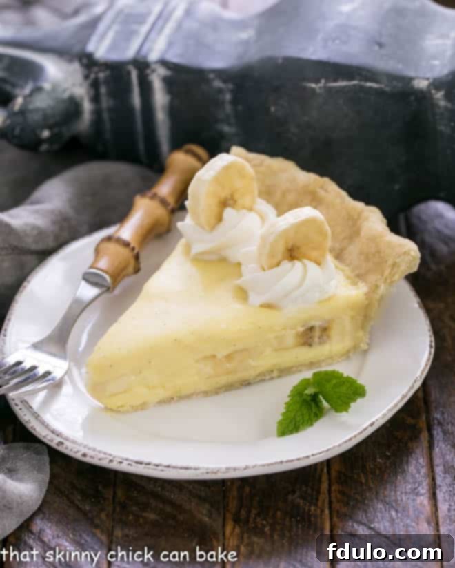 A perfectly portioned slice of the best banana cream pie on a white plate, subtly garnished with a fresh sprig of mint, ready to be savored.
