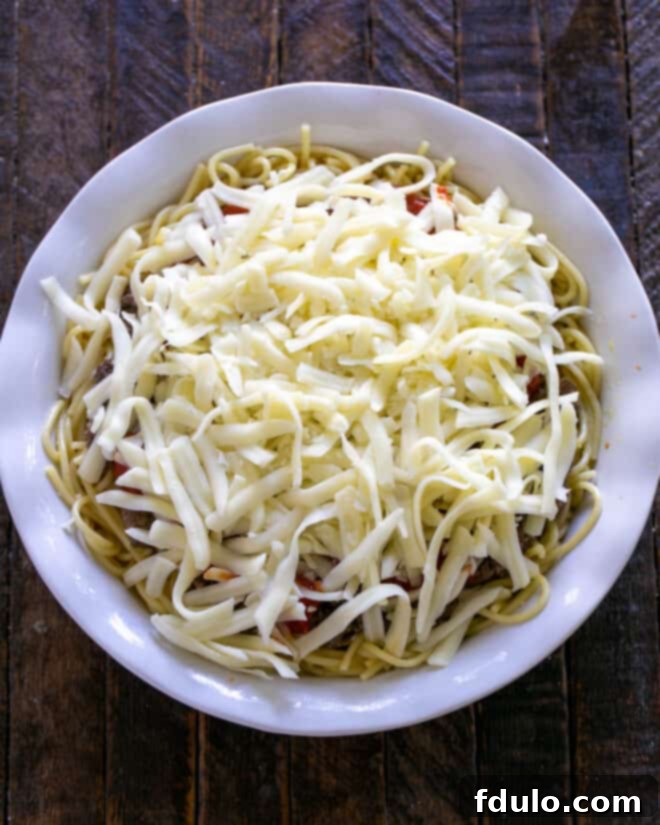 A generous amount of finely shredded mozzarella cheese is sprinkled abundantly over the marinara sauce, completely blanketing the top of the spaghetti pie, ready for baking until gloriously golden and bubbly.