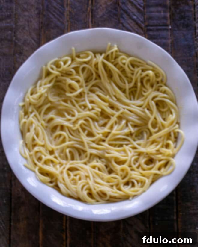 The egg-and-Parmesan-coated spaghetti is carefully pressed into a well-greased 9-inch pie plate, forming an even, compact layer on the bottom and extending up the sides, creating the pie's sturdy base.