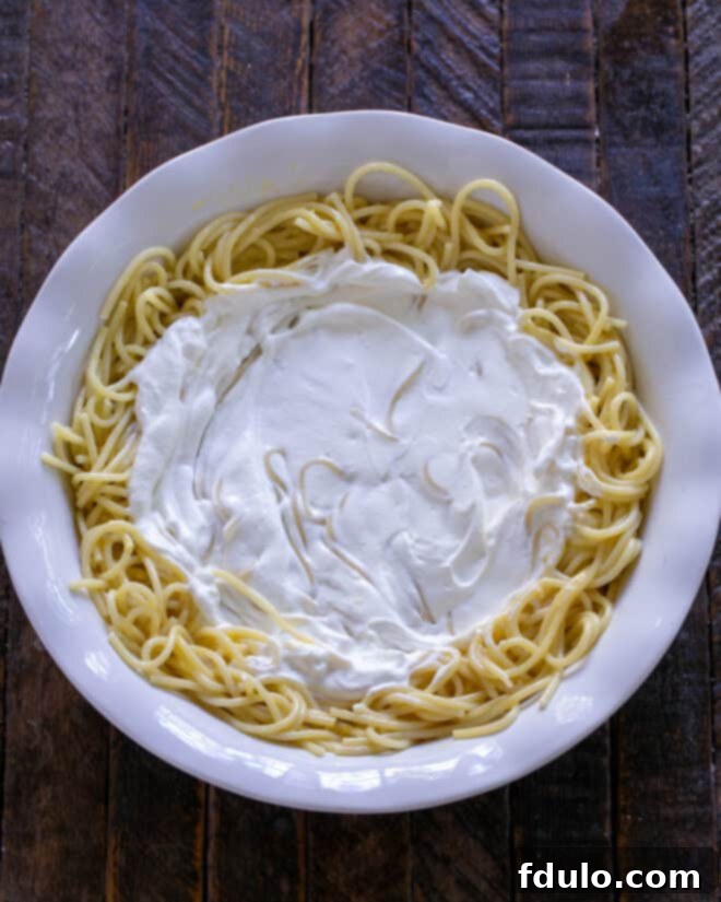 A generous, smooth layer of creamy sour cream is evenly spread over the spaghetti crust in the pie plate, creating a pristine, white foundation for the subsequent savory layers.