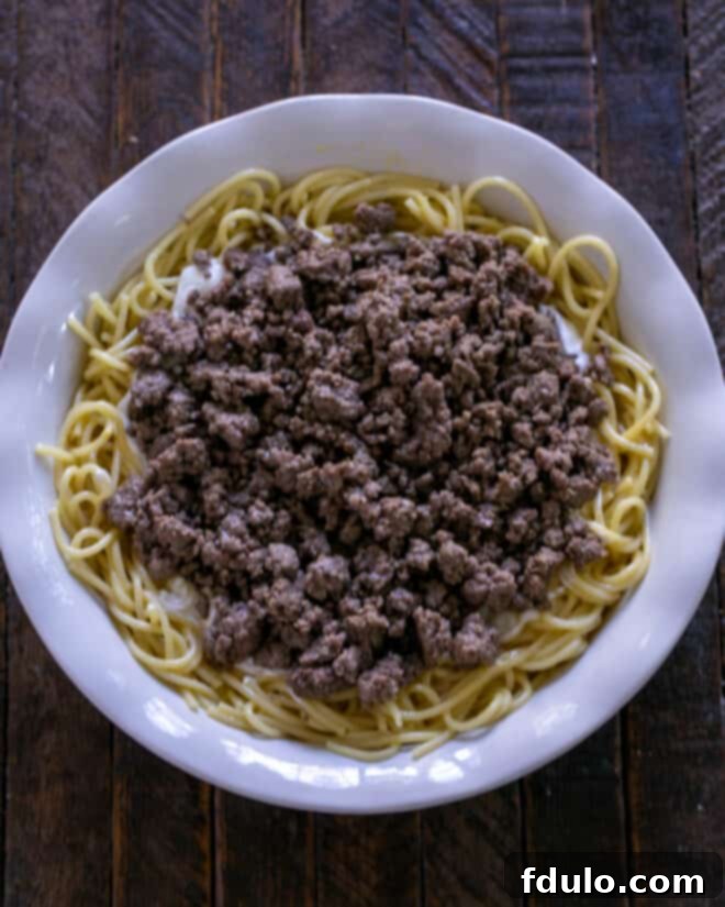 A hearty layer of perfectly seasoned, crumbled ground beef is spread evenly over the sour cream layer in the spaghetti pie, forming a substantial and savory filling.