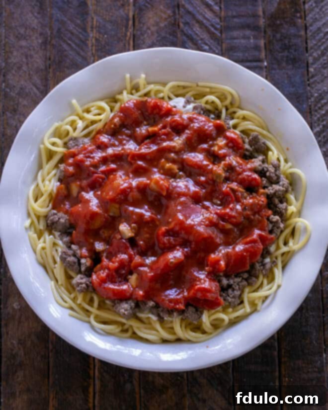 A rich, vibrant marinara sauce is carefully spooned over the ground beef layer in the spaghetti pie, ensuring full, even coverage and adding a burst of fresh, tangy tomato flavor.