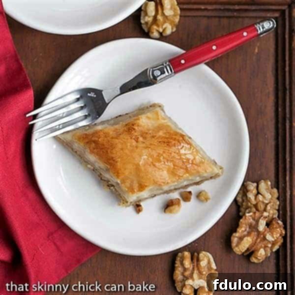Overhead view of a single slice of Classic Greek Baklava on a white plate, highlighting its golden-brown crispness and syrupy sheen.