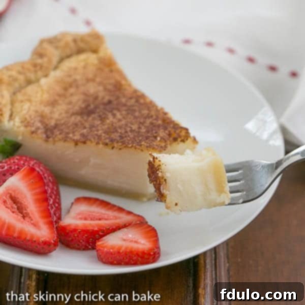 Sugar Cream Pie bite on a fork with pie slice and strawberries on a dessert plate in the background, showing a perfect bite.